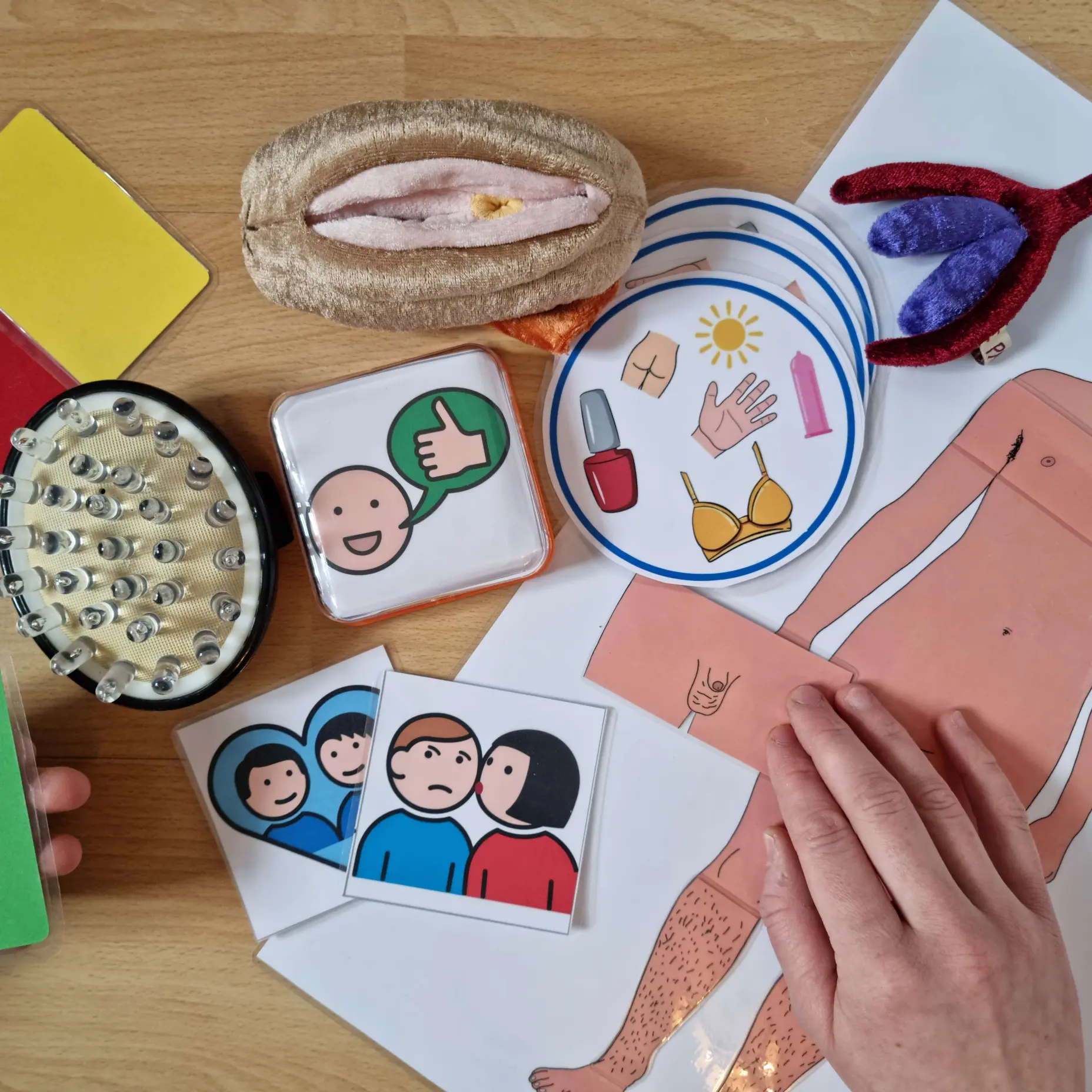 Materialien aus einem Workshop auf einem Tisch: Metacom-Symbolkarten, ein Körperumriss aus Papier, Tastmaterial und ein Stoffmodell.